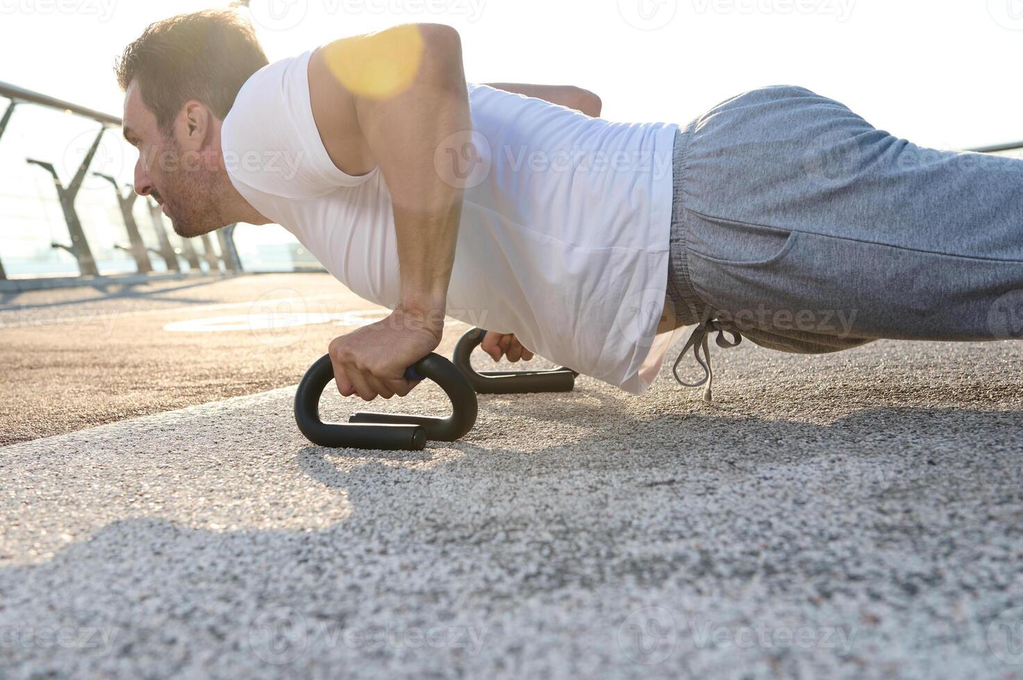 Close-up portrait of a handsome middle aged Caucasian man, muscular build athlete doing push ups during an outdoor workout on the city bridge early in the morning photo