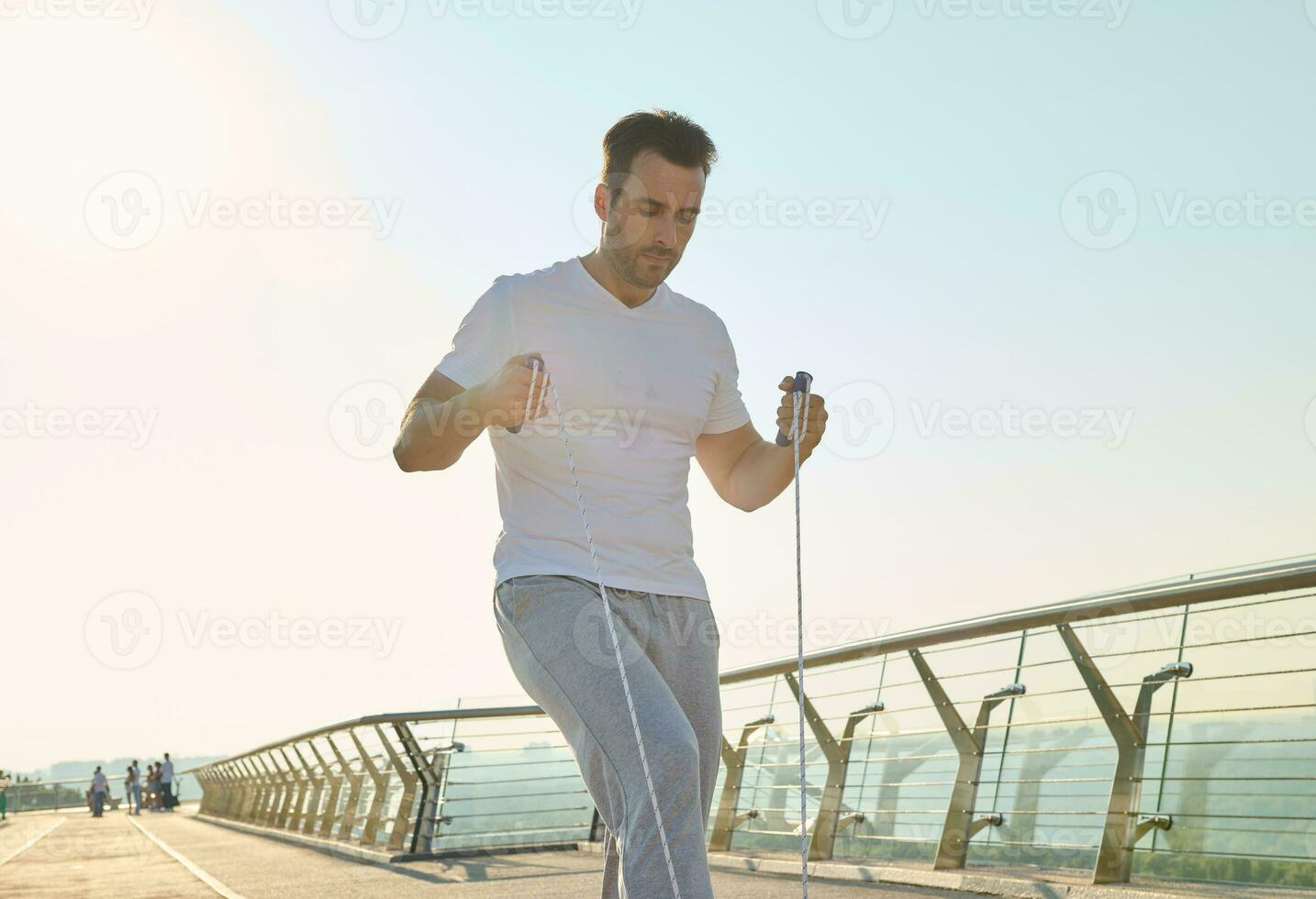 Handsome middle aged sportsman training with jumping rope on a city bridge treadmill early in the morning on a beautiful sunny summer day. Keep your body fit photo