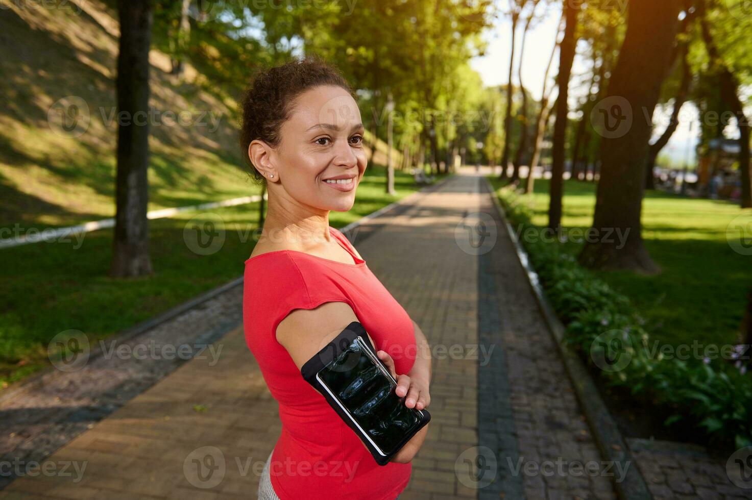 Portrait of a confident 40 years old African American woman in sportswear standing in forest city park with her arms crossed and smiling with a beautiful toothy smile during her morning run or workout photo
