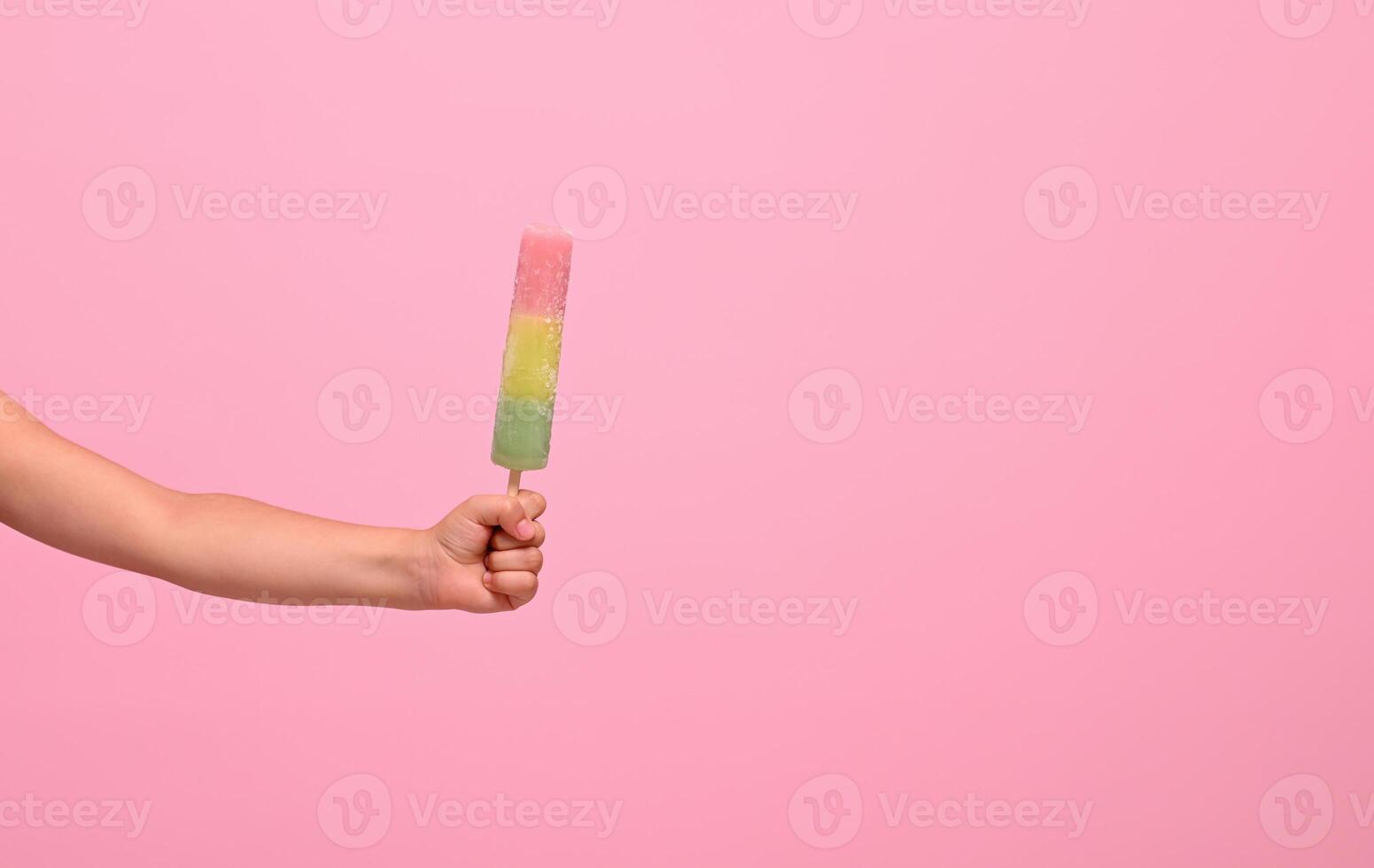 Healthy vegan ice cream popsicle in hand of a baby girl isolated on pink wall background with copy space . Summer dessert and cheerful summer mood concept photo