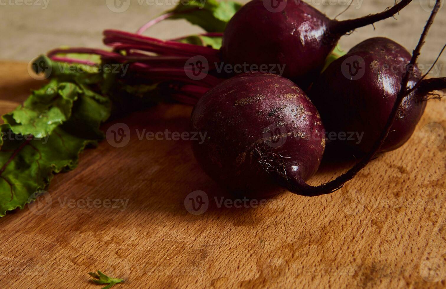 Close-up of a bunch of fresh burgundy beetroot with green tops and leaves on a wooden cutting board . Food background of seasonal raw vegetables photo