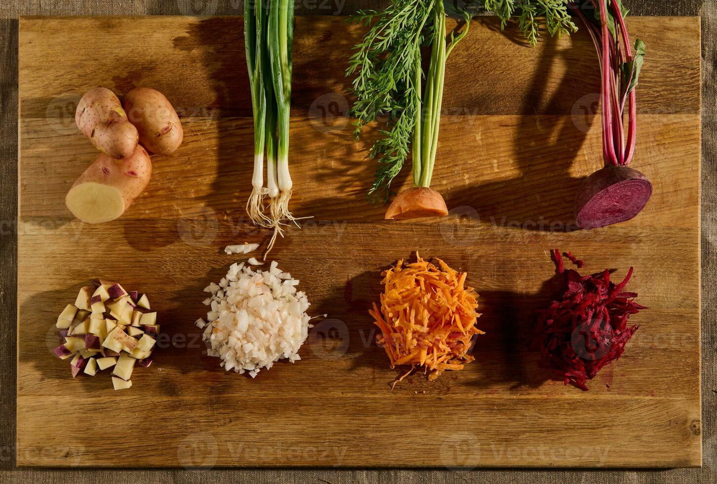 Top view of seasonal fresh raw vegetables on a wooden board, cut in half and the other half shredded on a grater. Beets, carrots, green onions with green leaves and potatoes photo