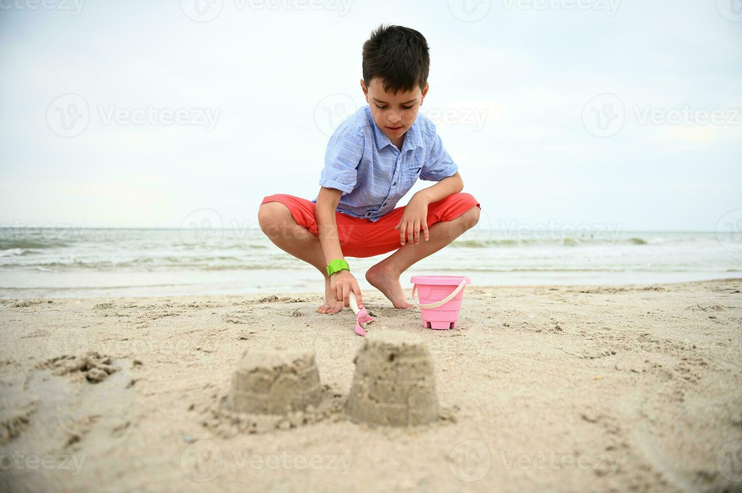 feliz, hermoso y adorable chico, niño, niñito relleno juguete Cubeta con arena para edificio castillos de arena a el playa. naturaleza, marina antecedentes. verano ocio actividades. foto
