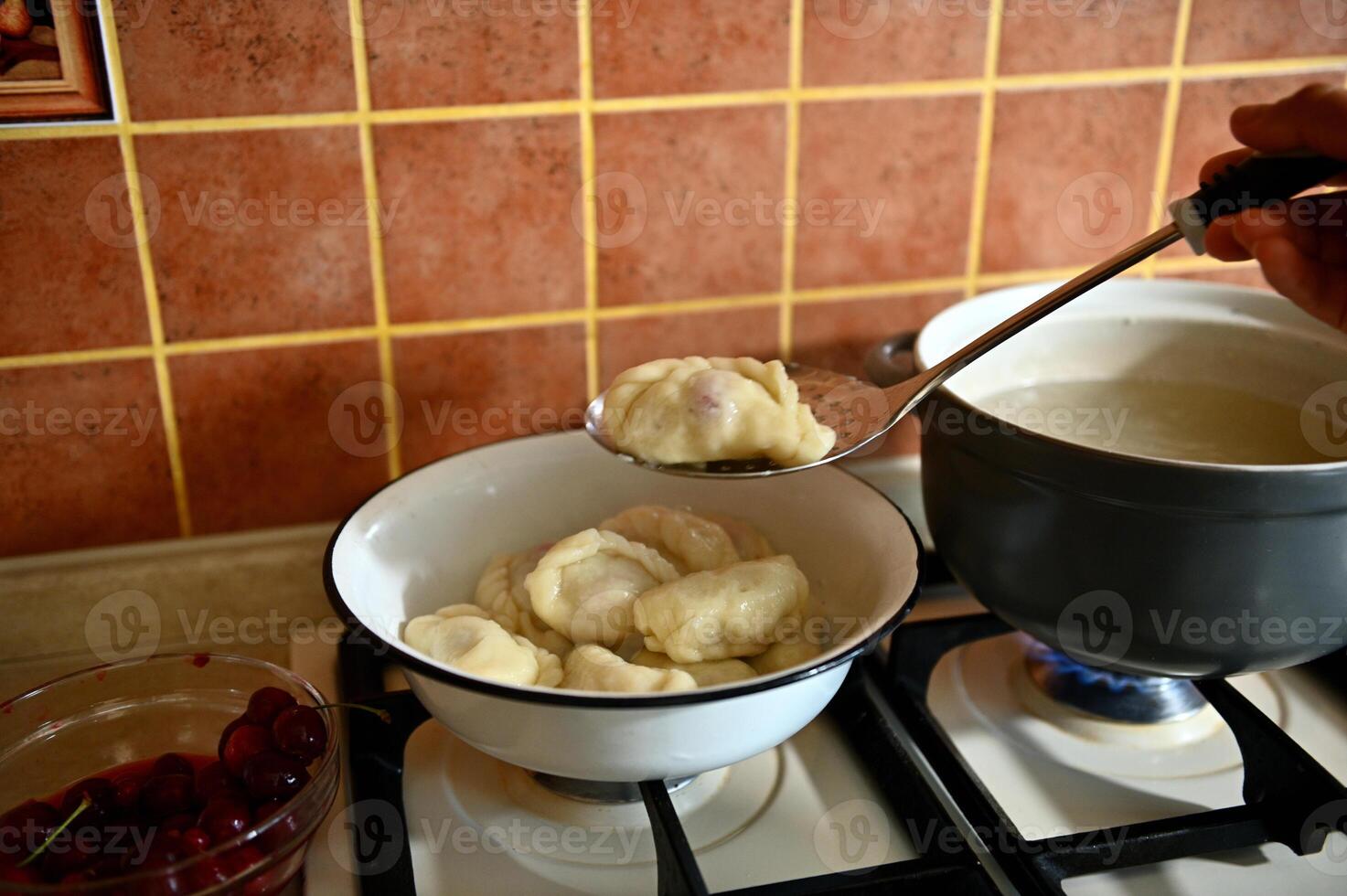 The pastry chef takes out cooked dumplings from boiling water into a colander photo