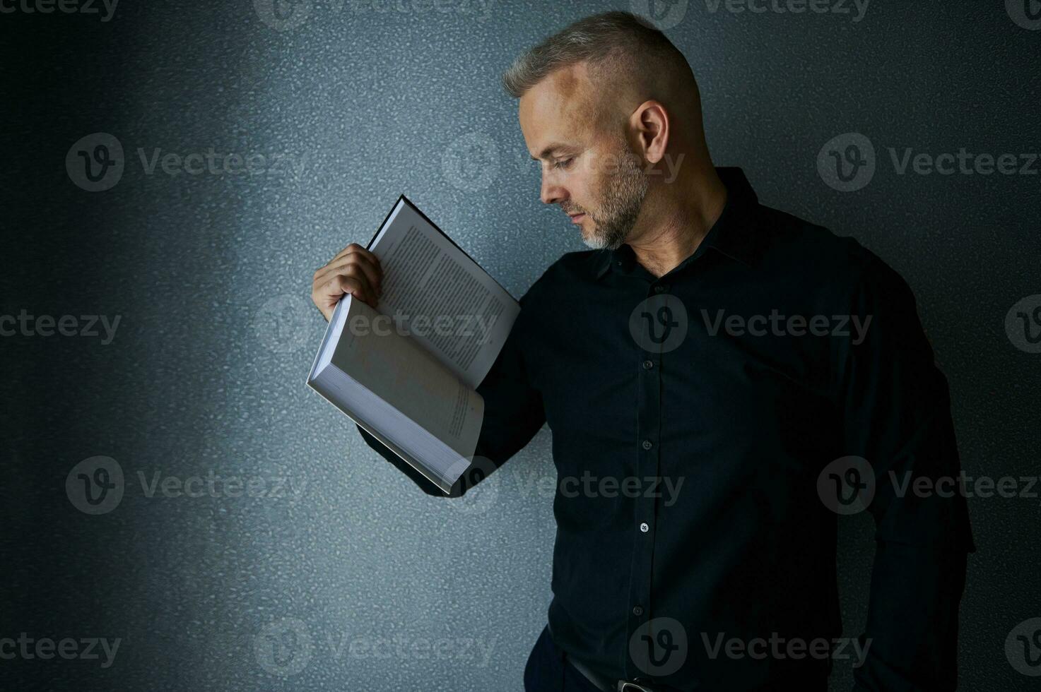 Portrait of an impressive imposing handsome stylish middle aged European man, successful businessman, entrepreneur holding a book in his hand and posing against gray wall background with copy space photo