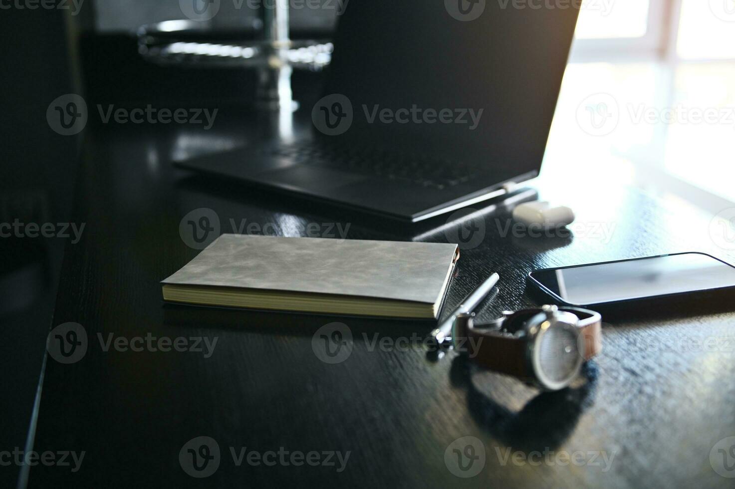 Close-up view of office accessories, laptop, earphones on the box, watch, mobile phone and gray notepad on wooden desk photo