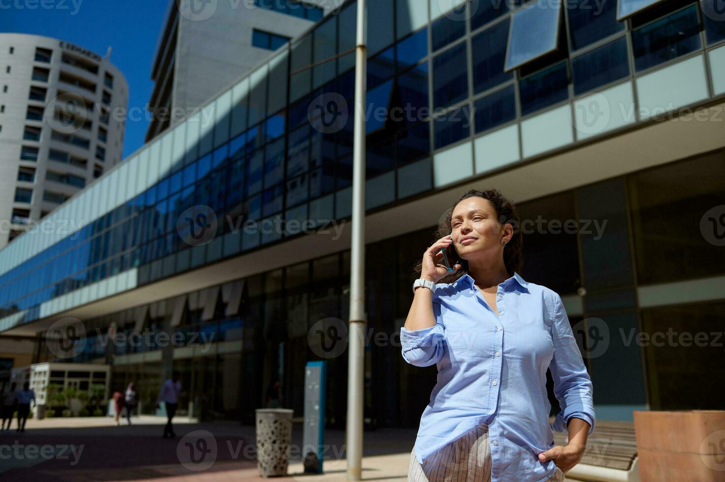 Authentic portrait of a multi-ethnic woman entrepreneur freelancer talking on smartphone against modern buildings photo