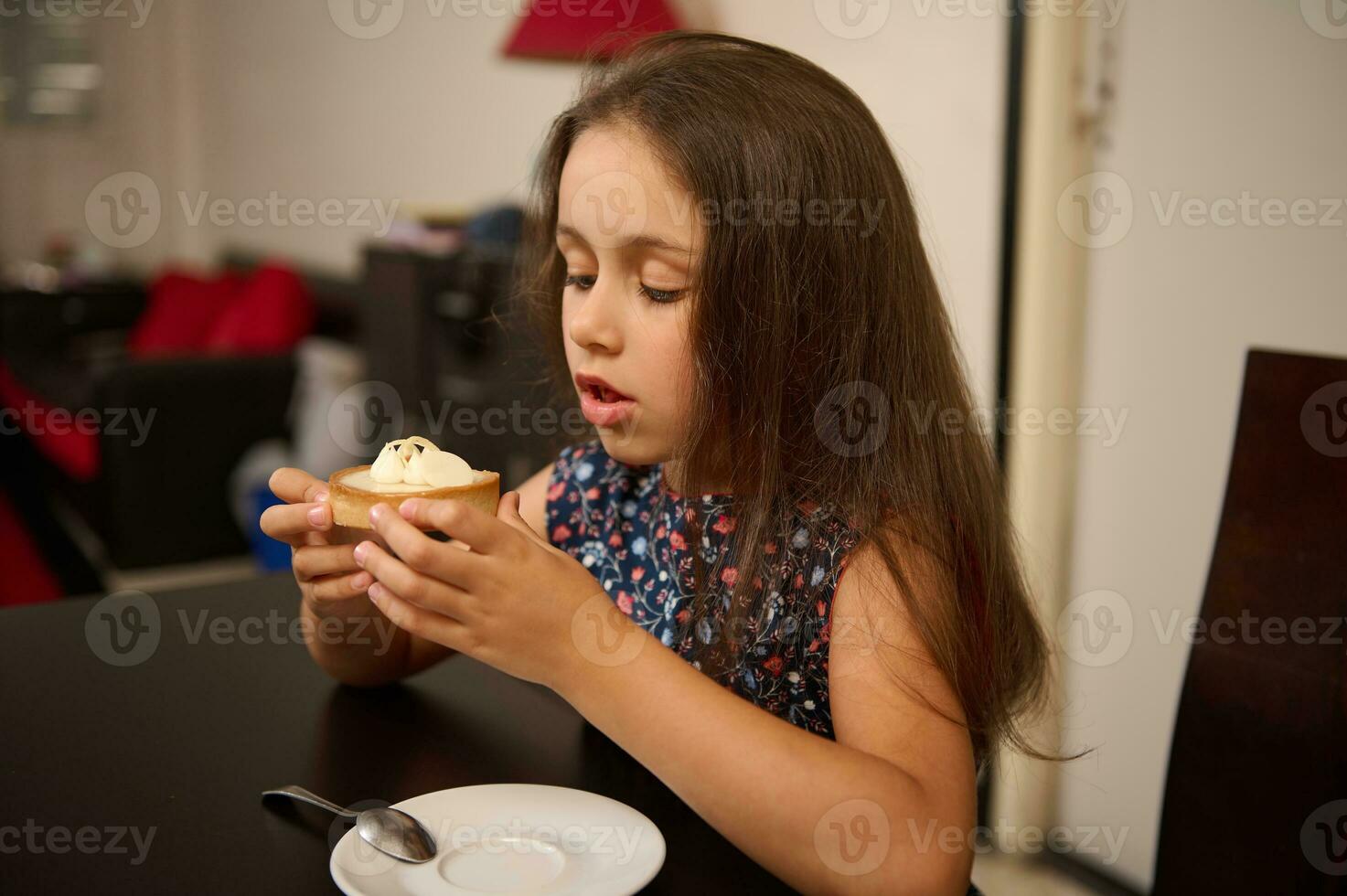 hermosa caucásico pequeño niña en elegante casual vestido, comiendo un delicioso limón pastel a hogar. dulce comida concepto foto