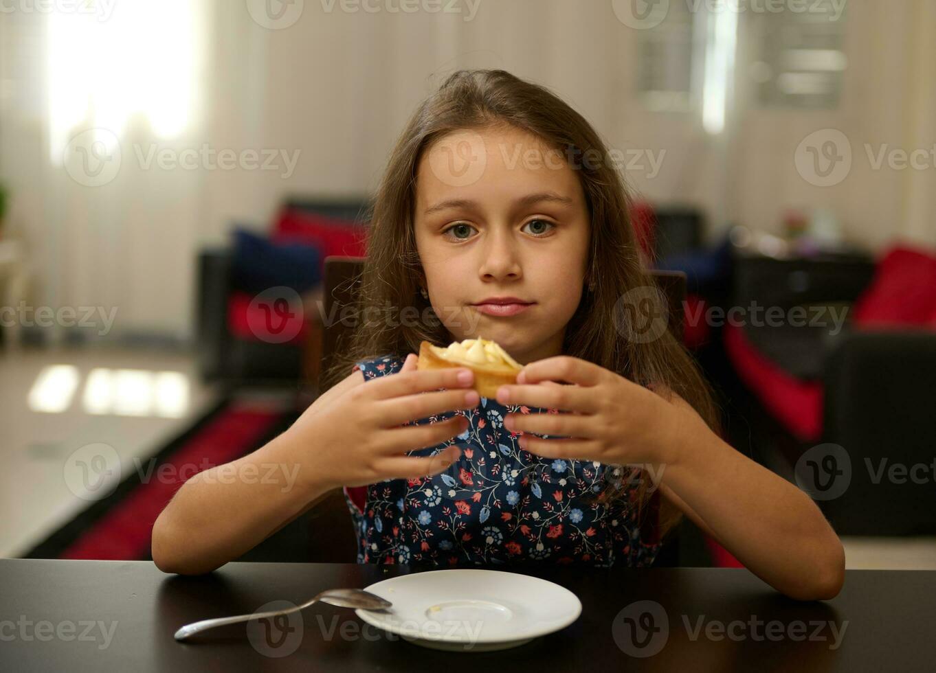 Adorable little child girl holding a sweet French dessert, smiling cutely and looking at camera photo