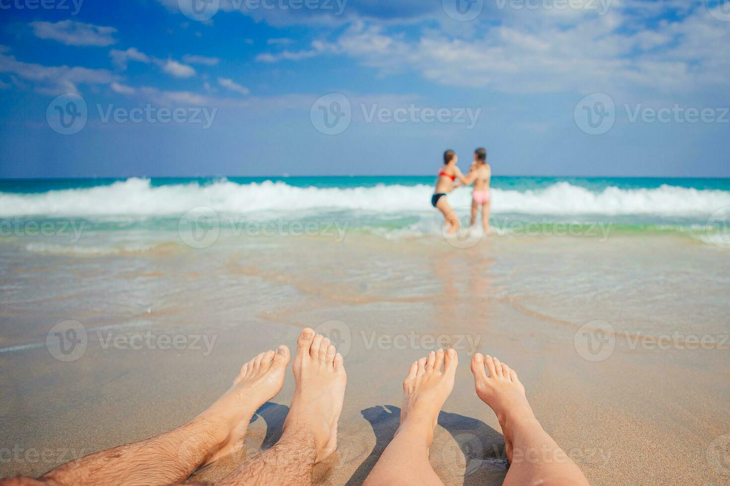 Closeup of the feet of family on the white sandy beach. Children play on the beach in shallow water on summer vacation photo