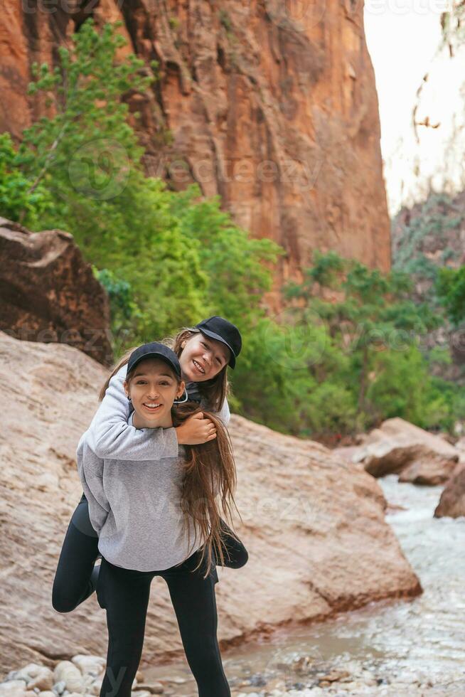 dos muchachas excursionismo en el montañas. Adolescente muchachas teniendo divertido y caminando en ruta en Sión nacional parque, Utah, Estados Unidos foto