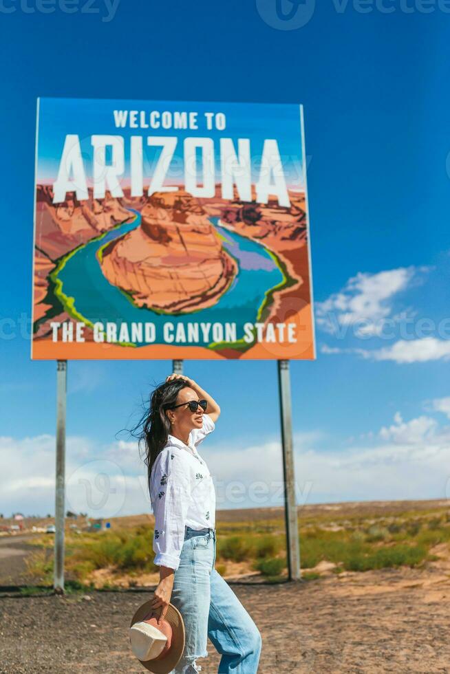 Beautiful woman on her trip to the USA on the background of Welcome to Arizona State border sign right in the Paje Canyon, USA photo
