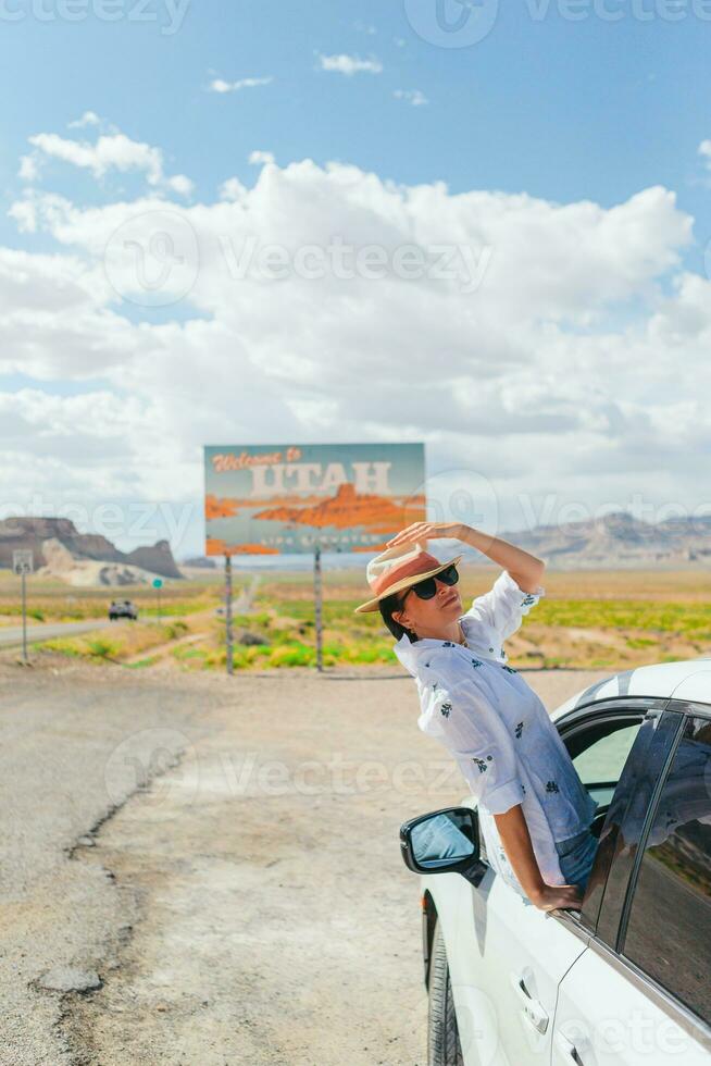 Beautiful woman on her trip by the car. Welcome to Utah road sign. Large welcome sign greets travels in Monument Valley, Utah photo