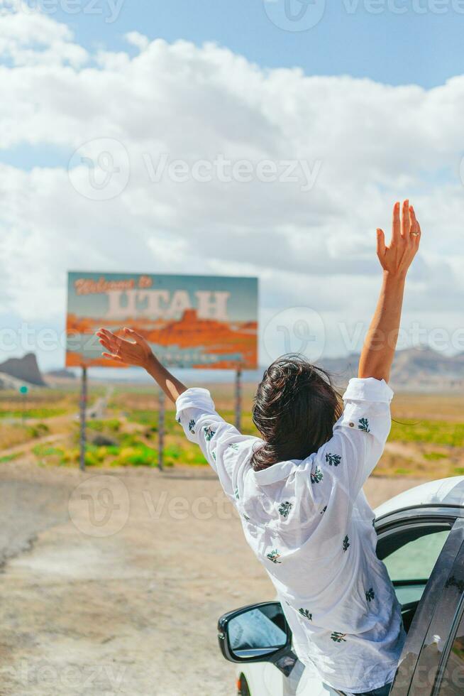Beautiful woman on her trip by the car. Welcome to Utah road sign. Large welcome sign greets travels in Monument Valley, Utah photo