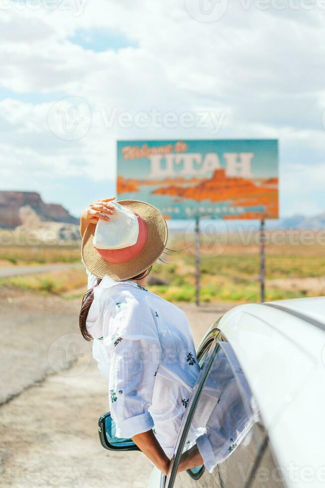 Beautiful woman on her trip by the car. Welcome to Utah road sign. Large welcome sign greets travels in Monument Valley, Utah photo