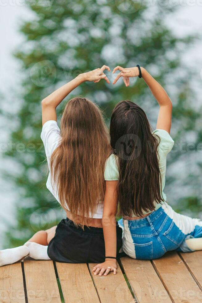 espalda ver de joven muchachas sentar en un terraza a un altura en el montañas en contra el fondo de niebla y montañas foto