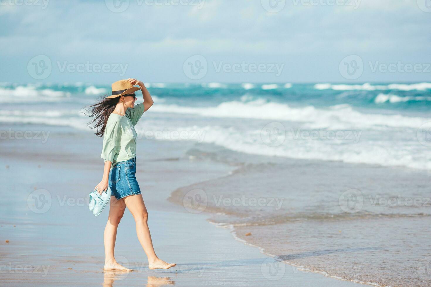 a woman in a hat and shorts standing on the beach photo