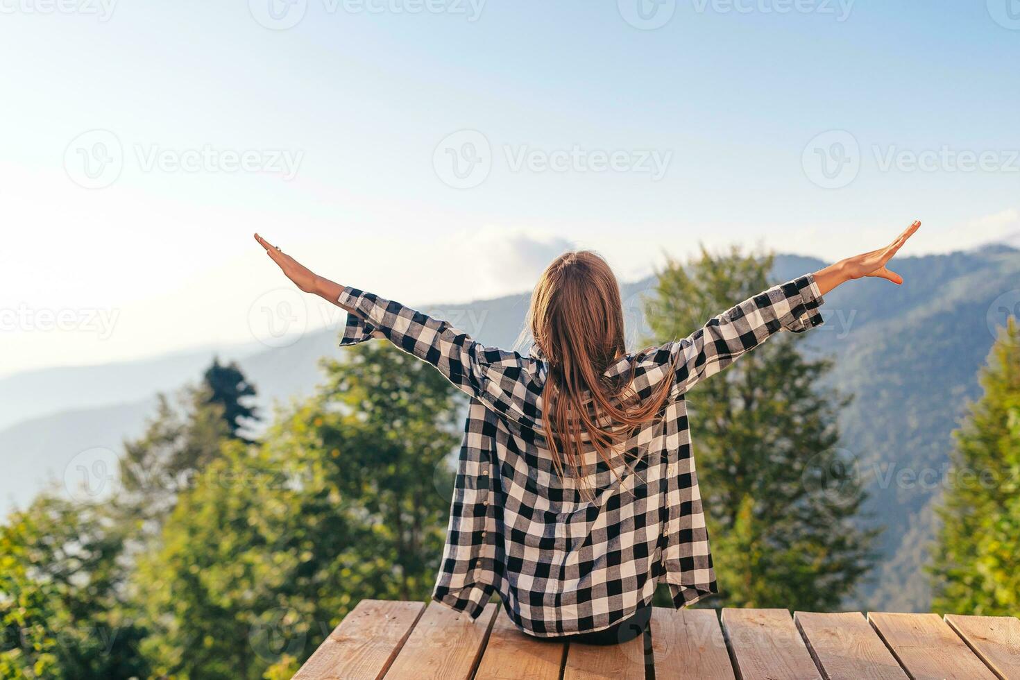 Back view of young girl sit on a terrace at a height in the mountains against the backdrop of fog and mountains photo