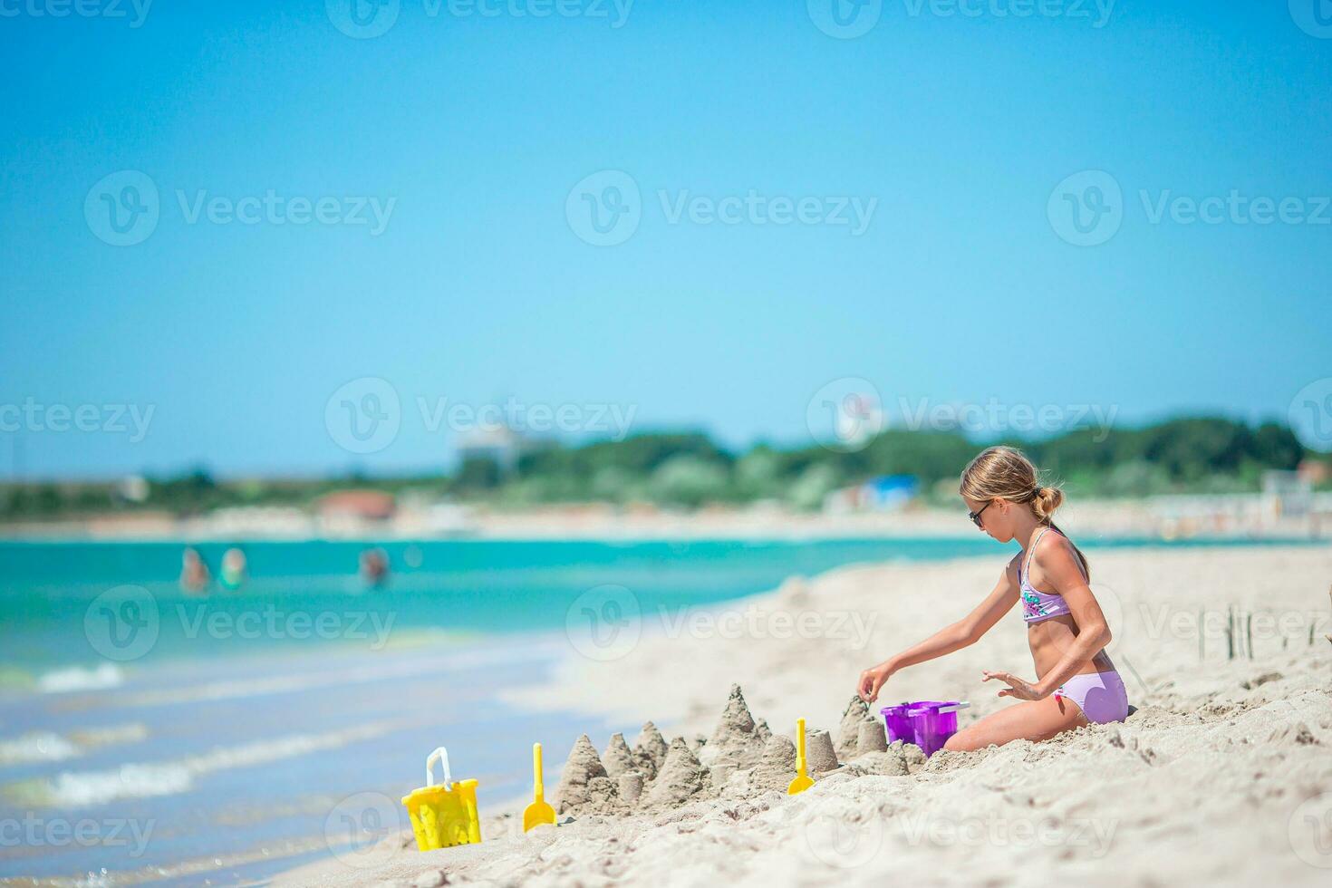 Little girl at tropical white beach making sand castle and playing with beach toys photo