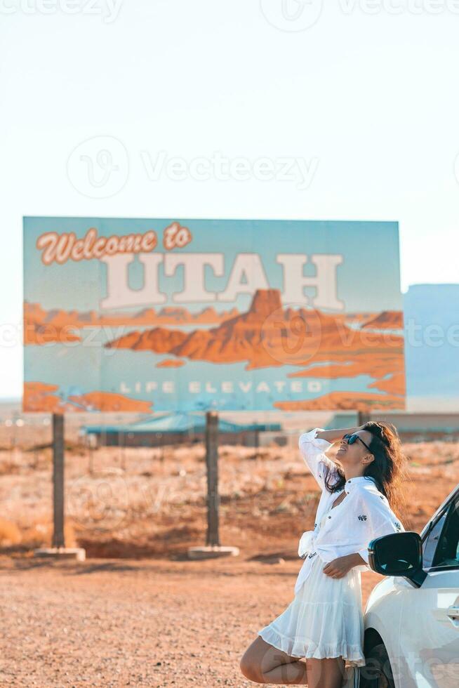 Beautiful woman on her trip by the car on the background of Welcome to Utah state border sign right in the Monument Valley photo