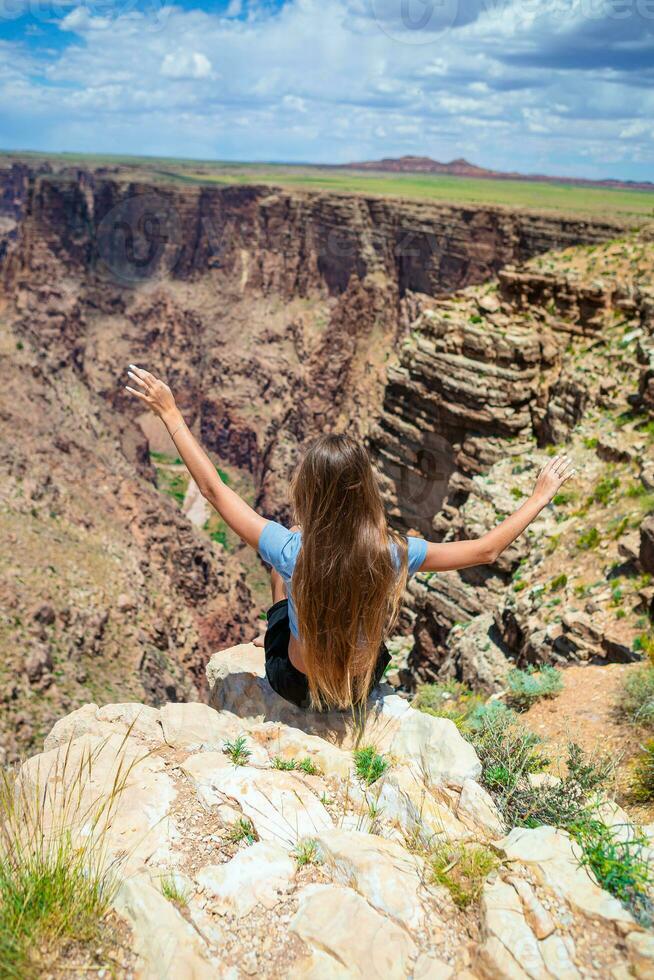 Back view of girl on a steep cliff taking in the amazing view over famous Grand Canyon on a beautiful sunny day, Grand Canyon National Park, Arizona, USA photo