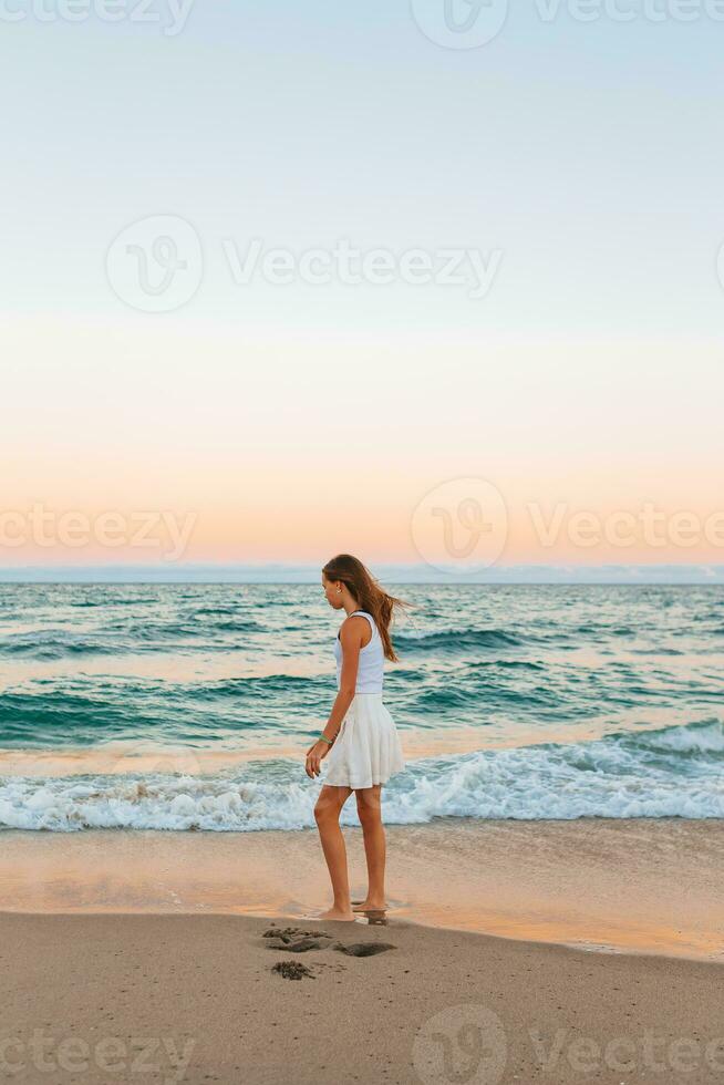 adorable adolescente niña en blanco en el costa durante su playa verano vacaciones con increíble cielo en antecedentes foto