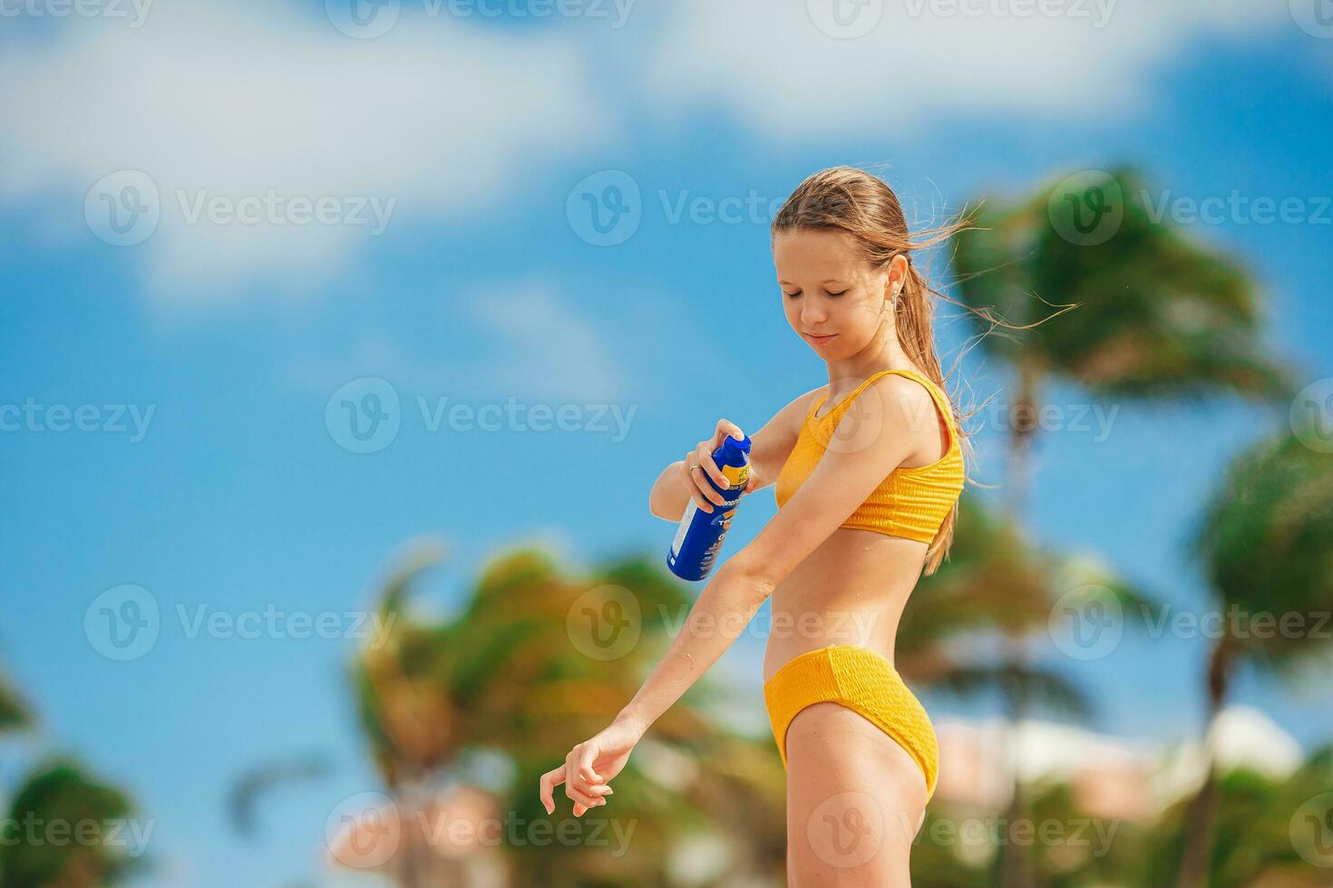 Adorable girl sprays protective cream on her body on a hot day. Sun protection photo