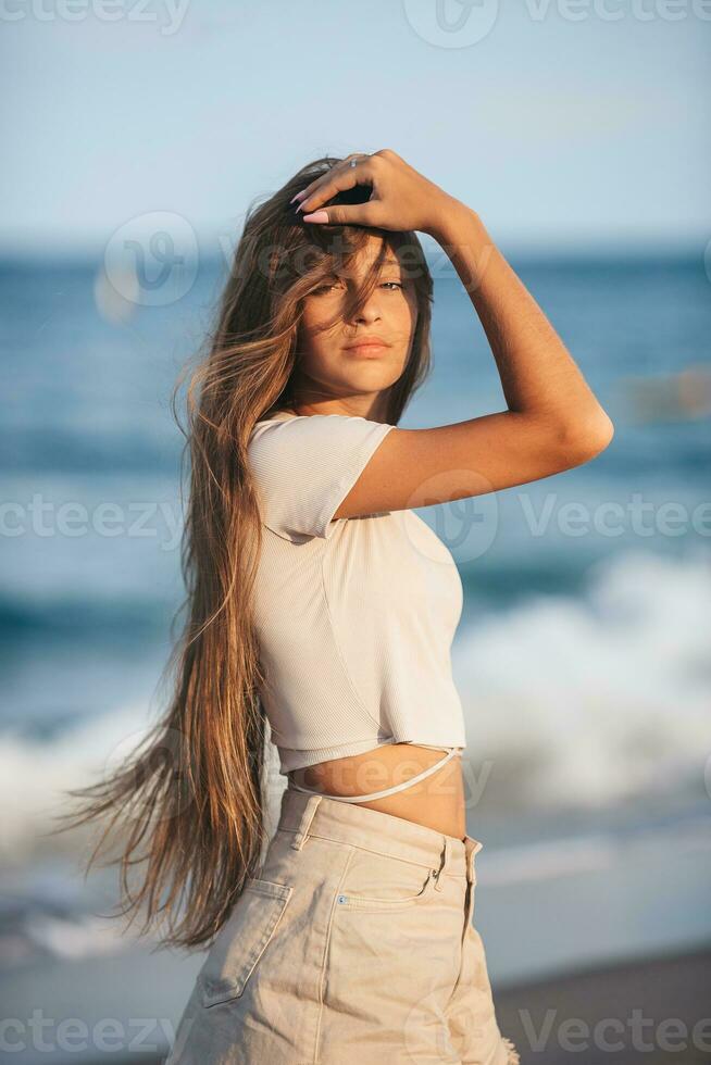 adorable joven niña con hermosa largo pelo disfrutar tropical playa vacaciones. el niña en el costa a puesta de sol foto