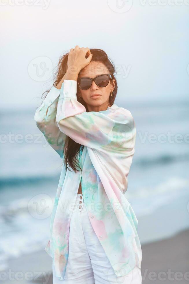 joven contento mujer en el playa disfrutar su verano vacaciones. mujer caminando a lo largo el mar en noche. foto