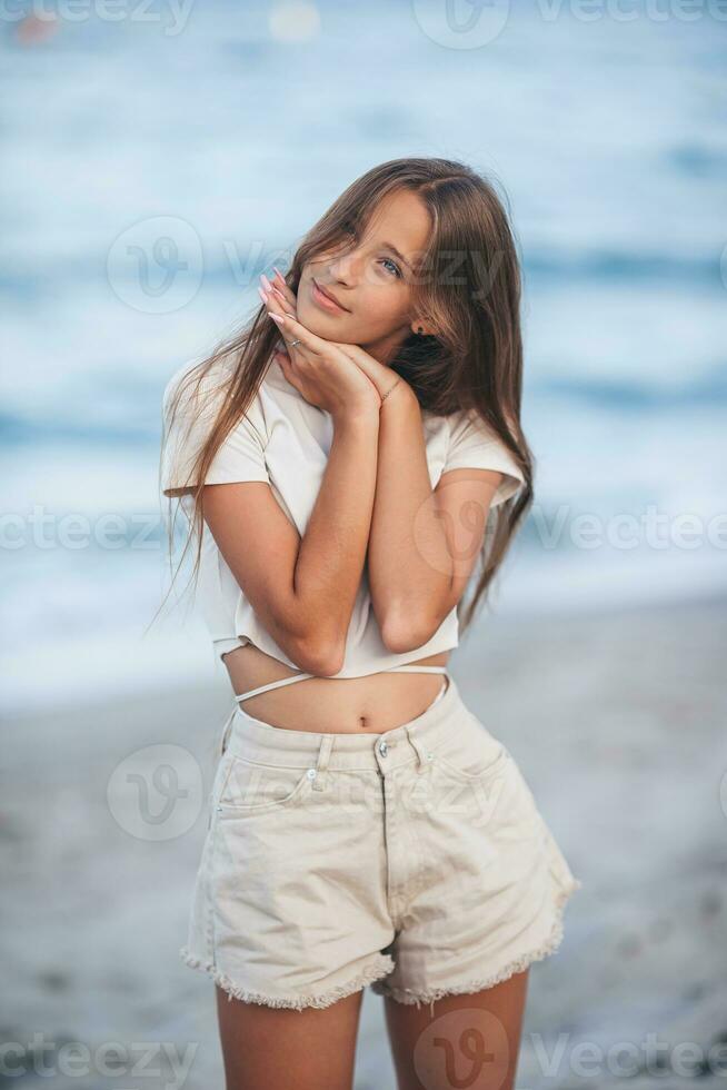 adorable joven niña con hermosa largo pelo disfrutar tropical playa vacaciones. el niña en el costa a puesta de sol foto