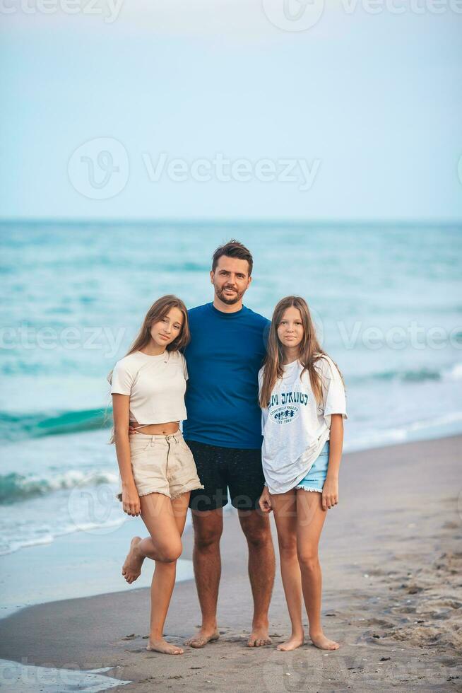 Portrait of father with his adorable daughters on the beach during their summer vacation photo