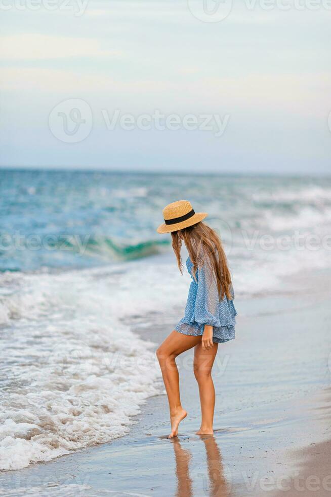 Adorable young girl with beautiful long hair enjoy tropical beach vacation. The girl on the seashore at sunset photo