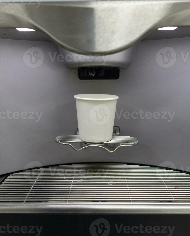 A paper coffee cup is placed on the sink of an automatic coffee machine. photo