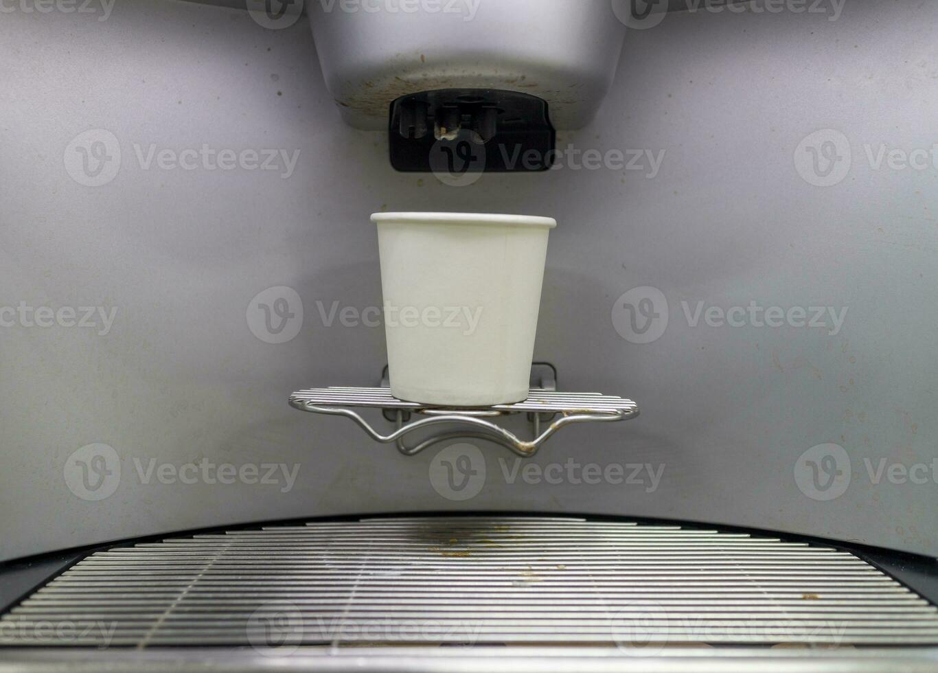 A paper coffee cup is placed on the sink of an automatic coffee machine. photo