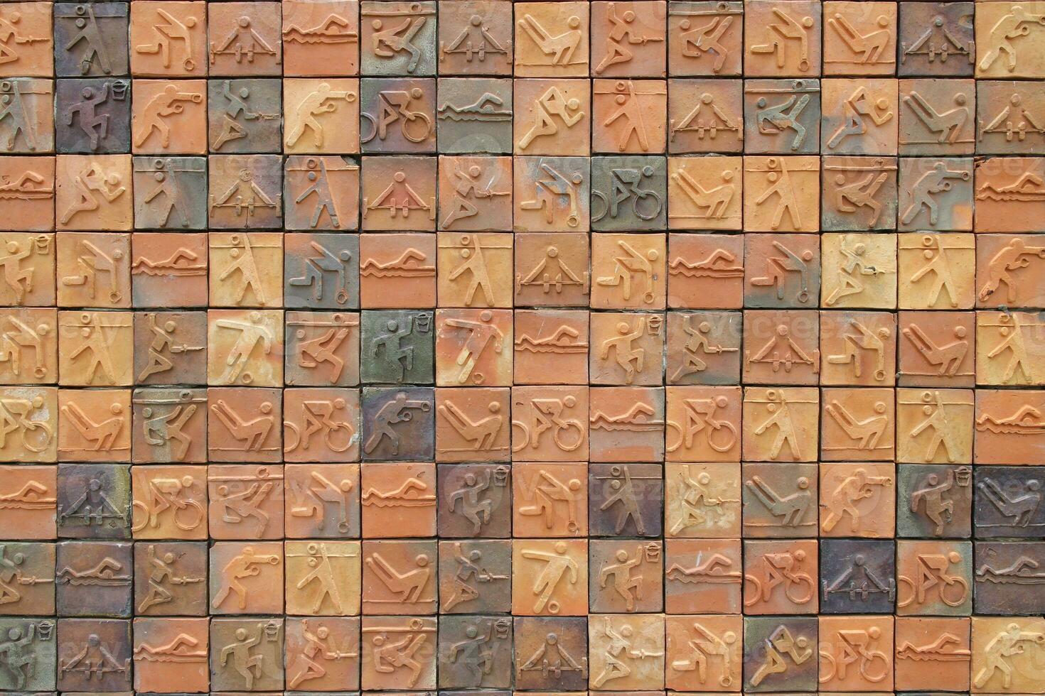 The brick wall of the building where each brick has a picture depicting a different sport. photo