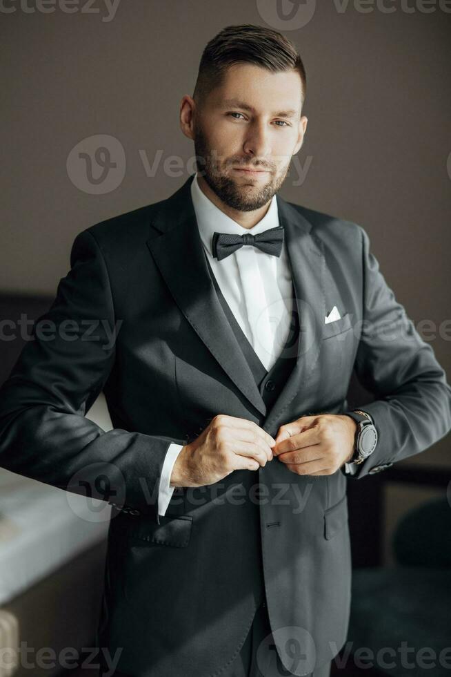 elegante novio retrato consiguiendo Listo en el Mañana para Boda ceremonia. Mañana de el novio. novio Mañana preparación. el novio pone un negro chaqueta. un grande retrato foto