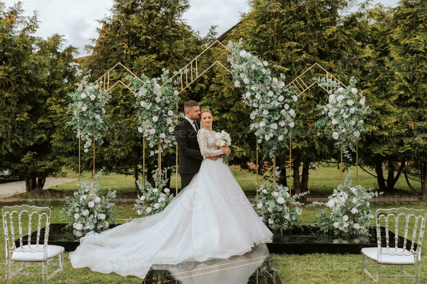 Attractive couple newlyweds, happy and joyful moment. Man and woman in festive clothes near the wedding decoration in boho style. Ceremony outdoors. photo