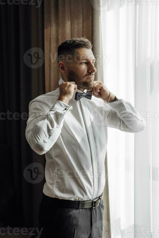 el elegante novio vestidos, prepara para el Boda ceremonia. grande retrato. maravilloso interior en el Mañana ligero. el del novio Mañana foto