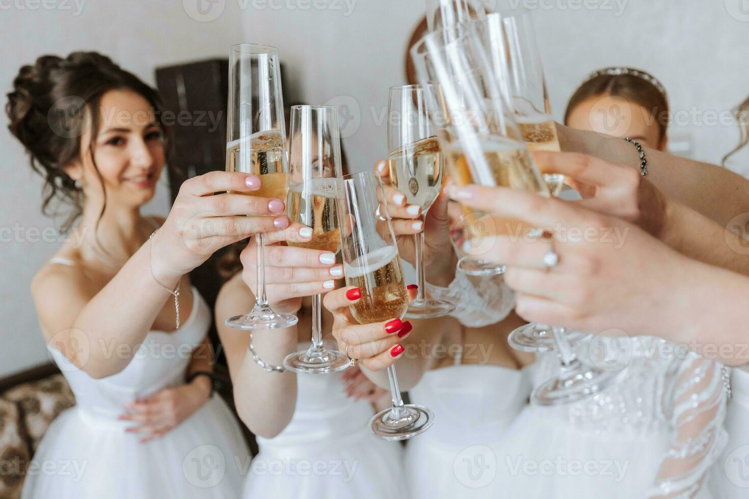 Bride with merry girlfriends at the wedding drink champagne from glasses. Bride and girlfriends hug in the room. Morning Bride and girlfriends. White dress. photo