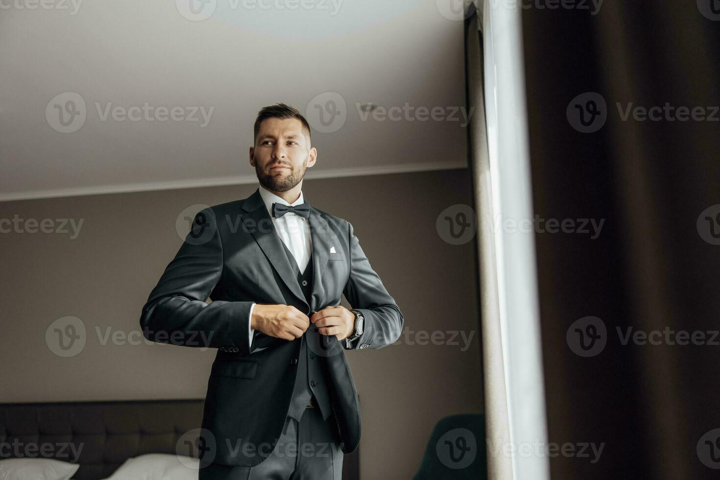 elegante novio retrato consiguiendo Listo en el Mañana para Boda ceremonia. Mañana de el novio. novio Mañana preparación. el novio pone un negro chaqueta foto