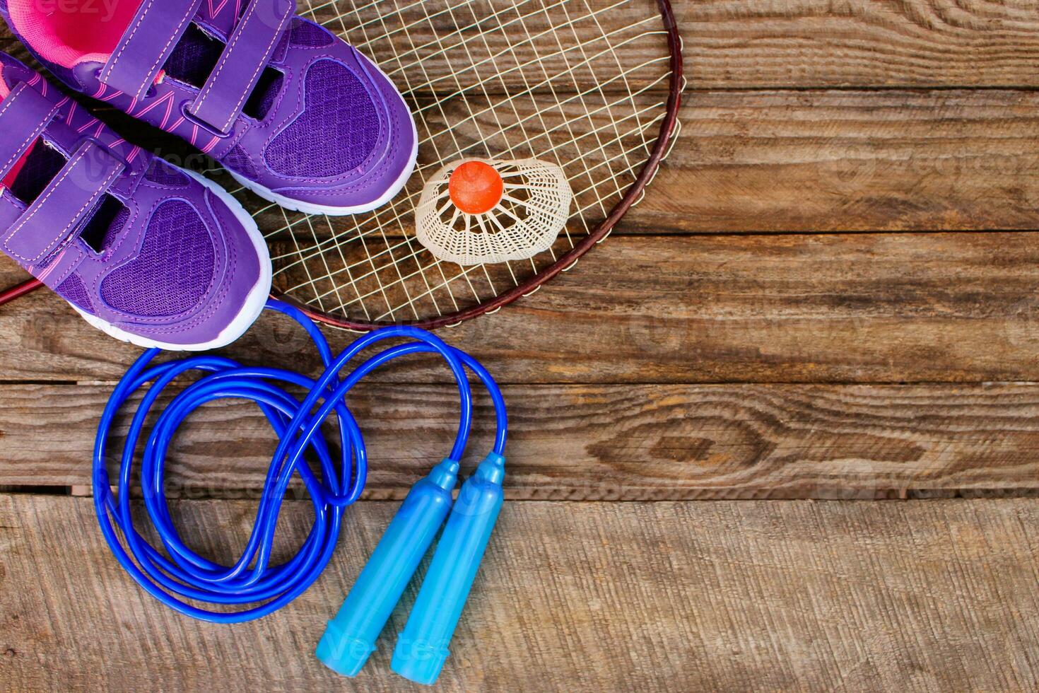 Sports equipment the birdie is on the racket, skipping rope, swimming goggles and sneakers on wooden background photo