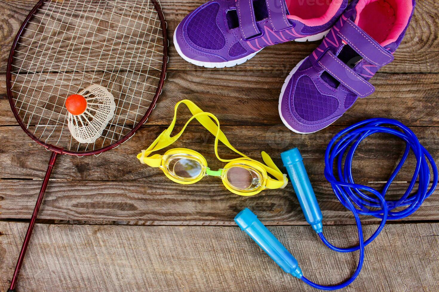 Sports equipment the birdie is on the racket, skipping rope, swimming goggles and sneakers on wooden background photo