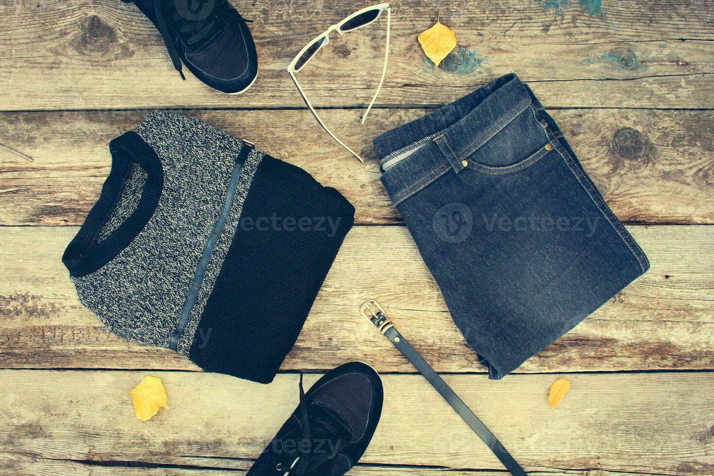 De las mujeres ropa y accesorios gris suéter, vaqueros, cinturón, zapatillas, Gafas de sol, amarillo hojas en de madera antecedentes. parte superior vista. tonificado imagen. foto