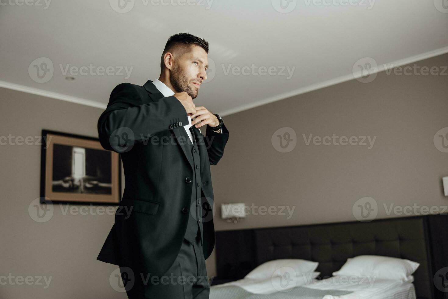 Stylish groom portrait getting ready in the morning for wedding ceremony. Morning of the groom. Groom morning preparation. The groom puts a black jacket in motion photo