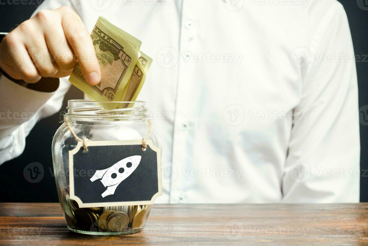 A man puts money into a startup jar. Research and development. Crowdfunding. Fundraising, financing with investment in promising projects and ideas. Entrepreneurship. Saving on a flight into space photo