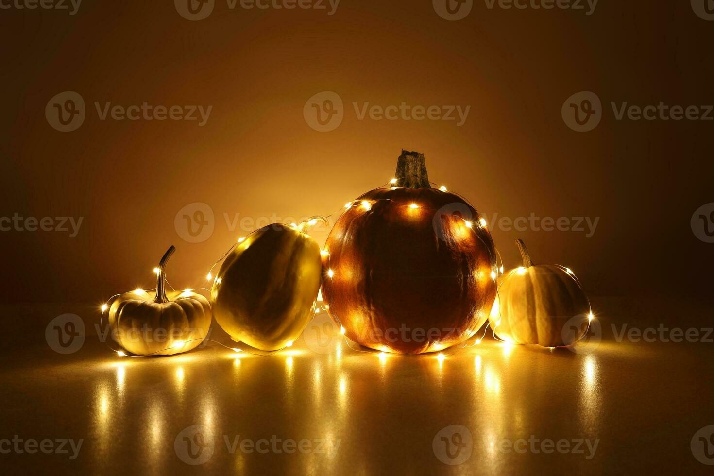 Four little pumpkins wrapped around a string lights garland on background highlighted yellow with shadows. Festive holidays Thanksgiving and Halloween decor concept. Place for text. photo