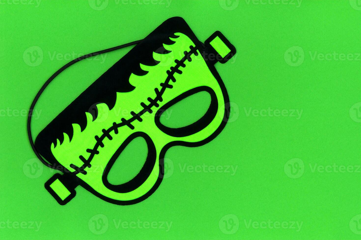 Bright green Frankenstein monster face carnival mask for Halloween masquerade party. Mask from costume store. Green background with space for text. Happy holiday and trick or treat concept photo. photo