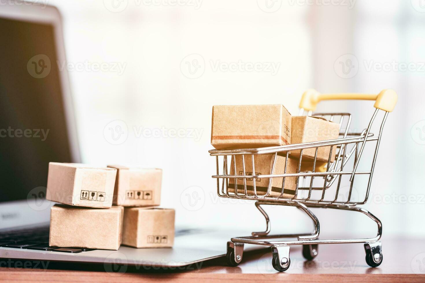 Brown parcel boxes on the laptop and in the shopping cart are positioned on a wooden table for the concept of online shopping, convenience and purchases arriving at doorstep. photo