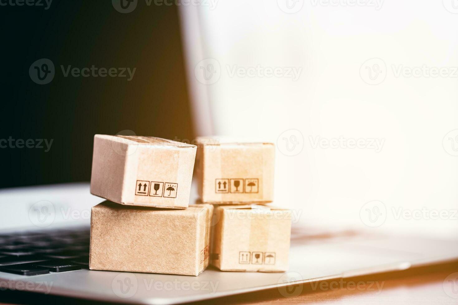 Brown parcel boxes are arranged on a laptop with a soft, gentle orange sunlight from the outside for the concept of online shopping, convenience and purchases arriving at doorstep. photo