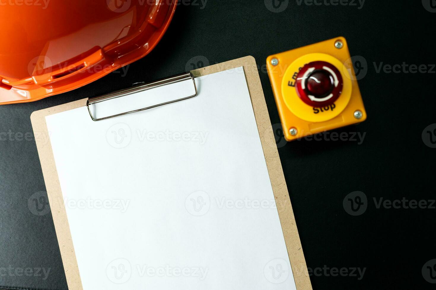 Blank clipboard paper, Emergency stop button and hard hat or safety helmet isolated on black background. photo